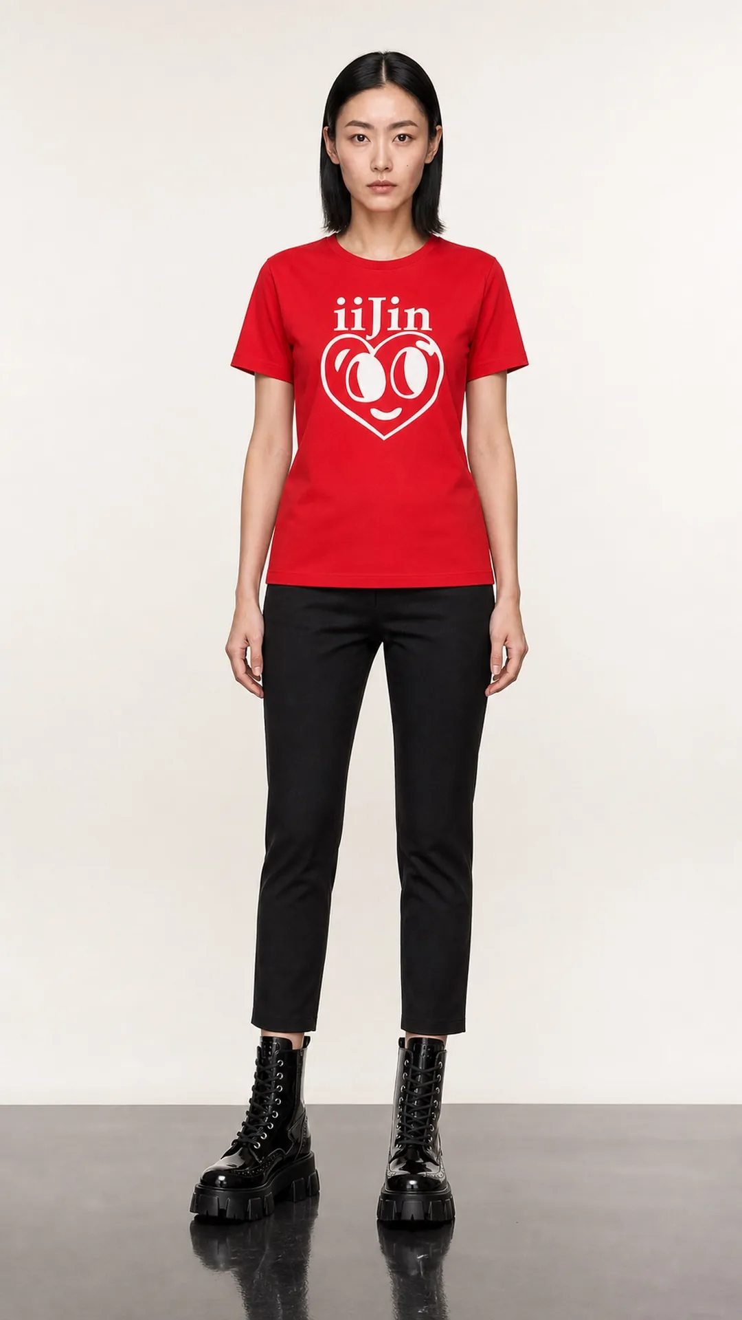 A model in a red iiJin printed tee, black cropped trousers and heavy black platform combat boots, standing full length on a pale seamless backdrop, lit to make the boots read as architecture.